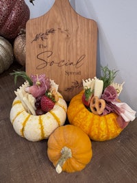 a wooden cutting board with pumpkins and cheese on it